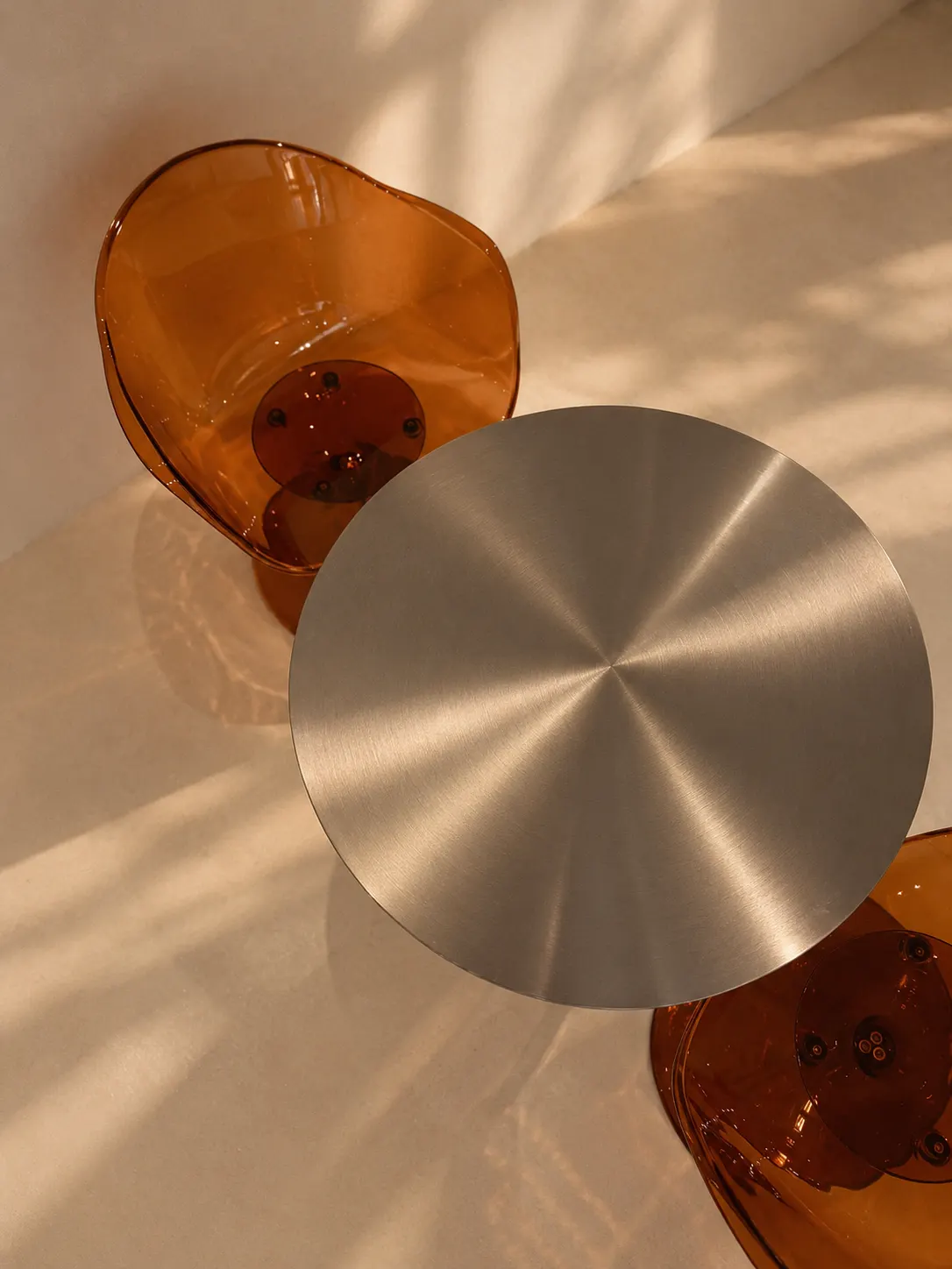 Overhead detail of an amber acrylic chair and brushed steel table top